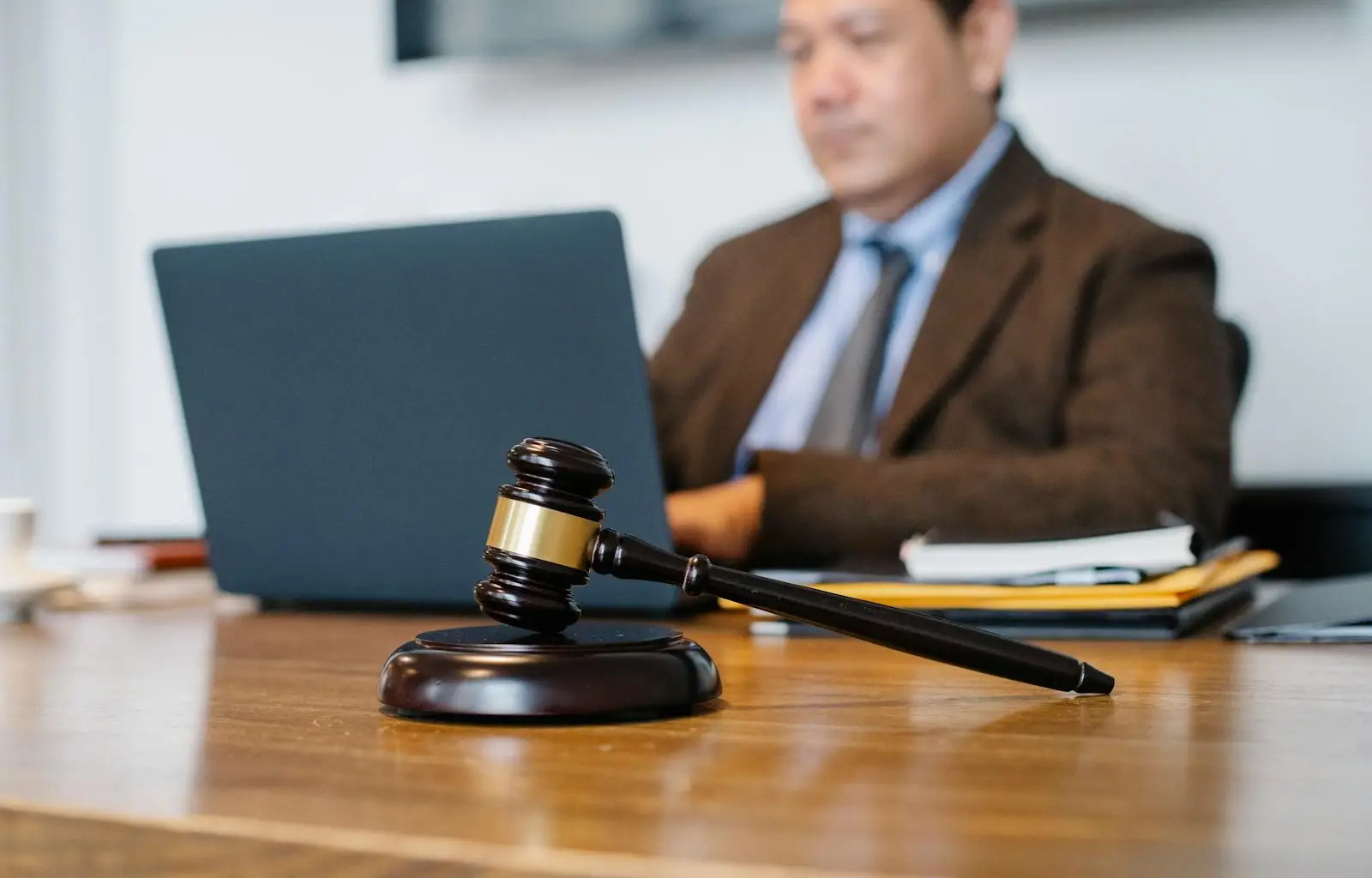 Crop concentrated Asian male judge in formal clothes sitting using modern netbook while working in law office