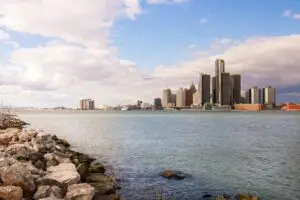 View of the Detroit skyline across the river on a clear day with rock-strewn waterfront.