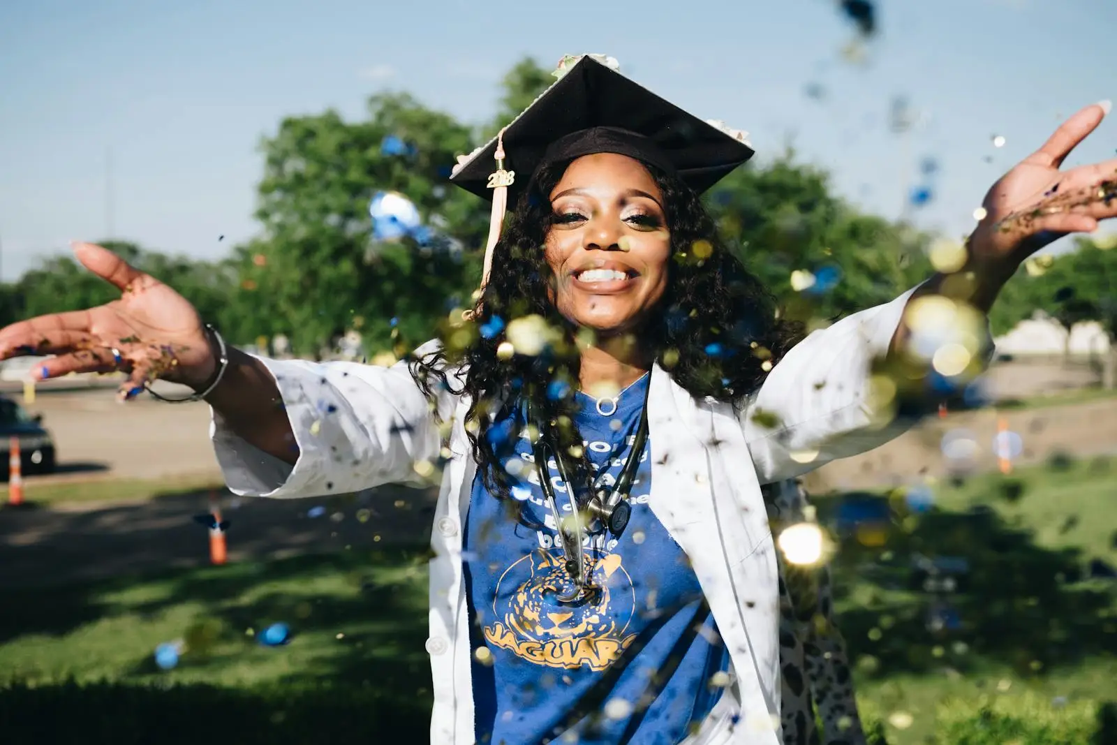 African American woman celebrating graduation with confetti outdoors, filled with happiness and success.