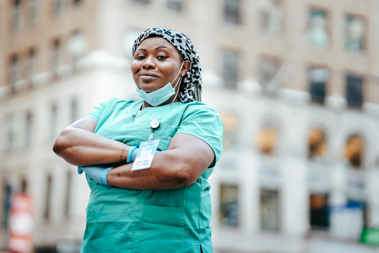 Proud Physician Assistant with arms crossed, in uniform, outdoors, urban setting, showing confidence and professionalism.